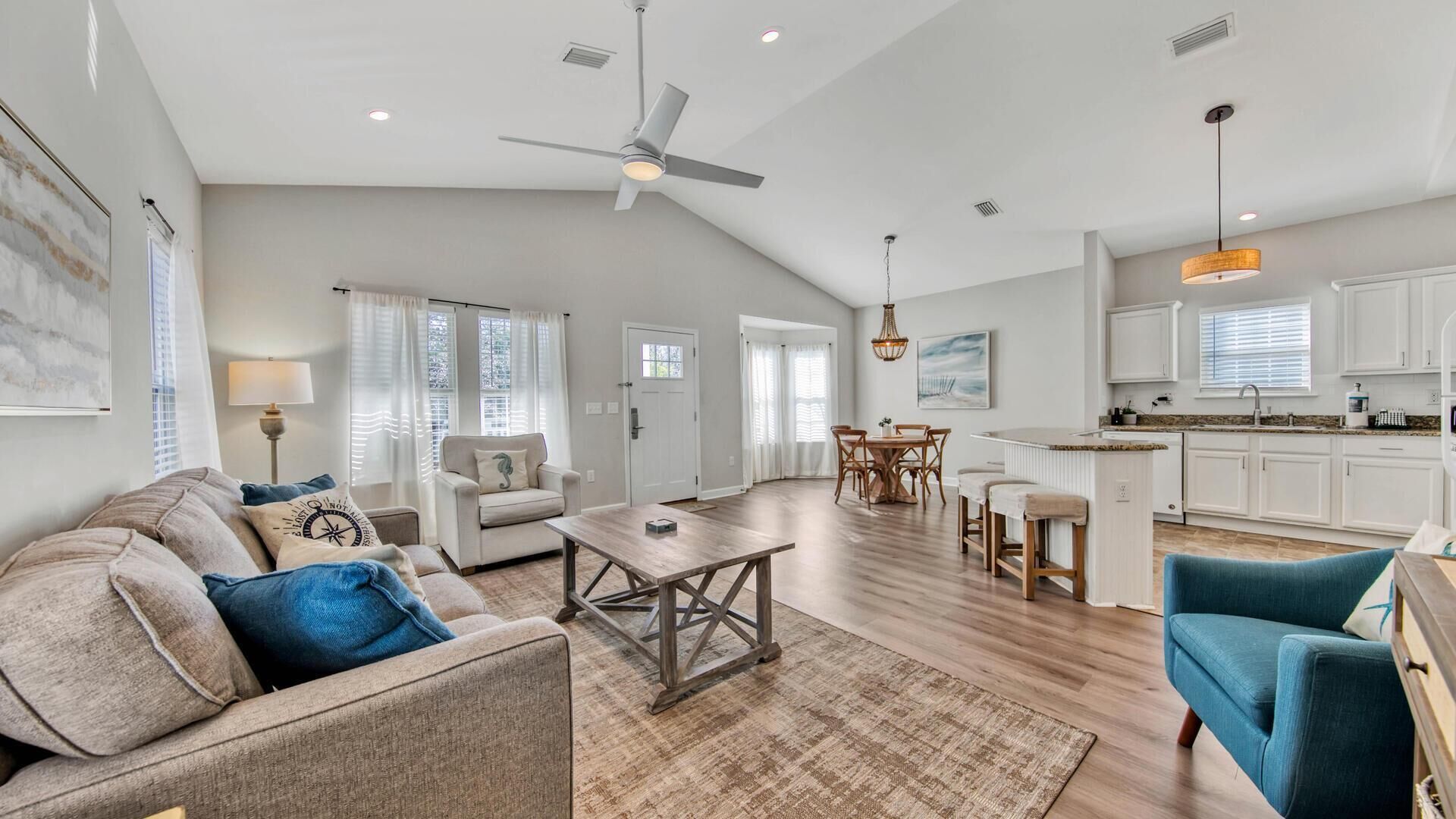 A spacious living area with a high ceiling, a dining table, and a kitchen area with white cabinets.