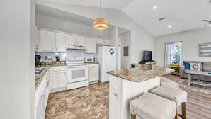 A modern kitchen with white cabinets, a granite countertop, and a central island with bar stools. - Beach Bum Hideaway (Santa Rosa Beach)