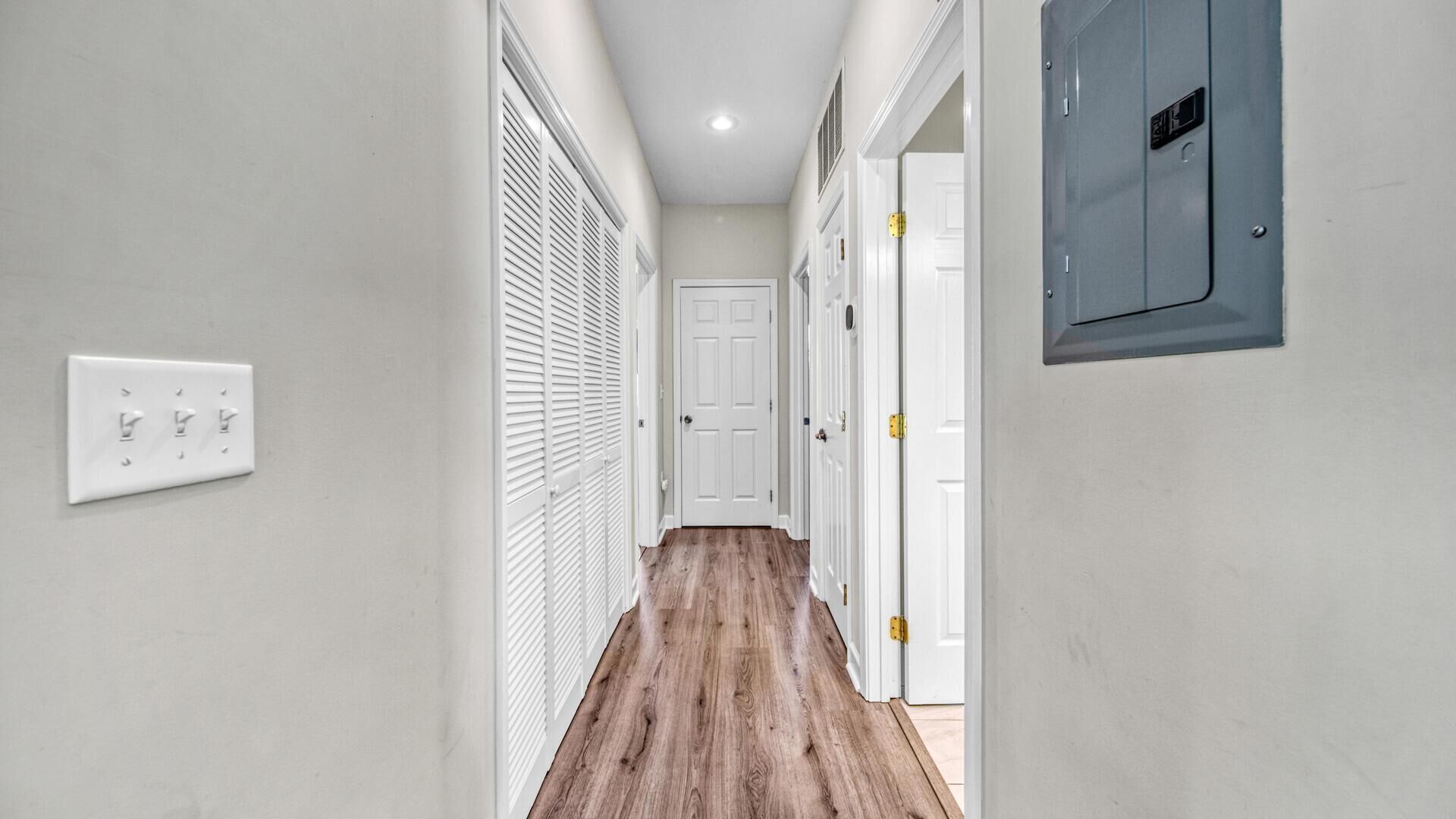 A narrow hallway with white walls, a wooden floor, and a white door at the end.