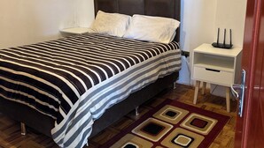 Un dormitorio con cama, mesita de noche, lámpara y alfombra estampada.
