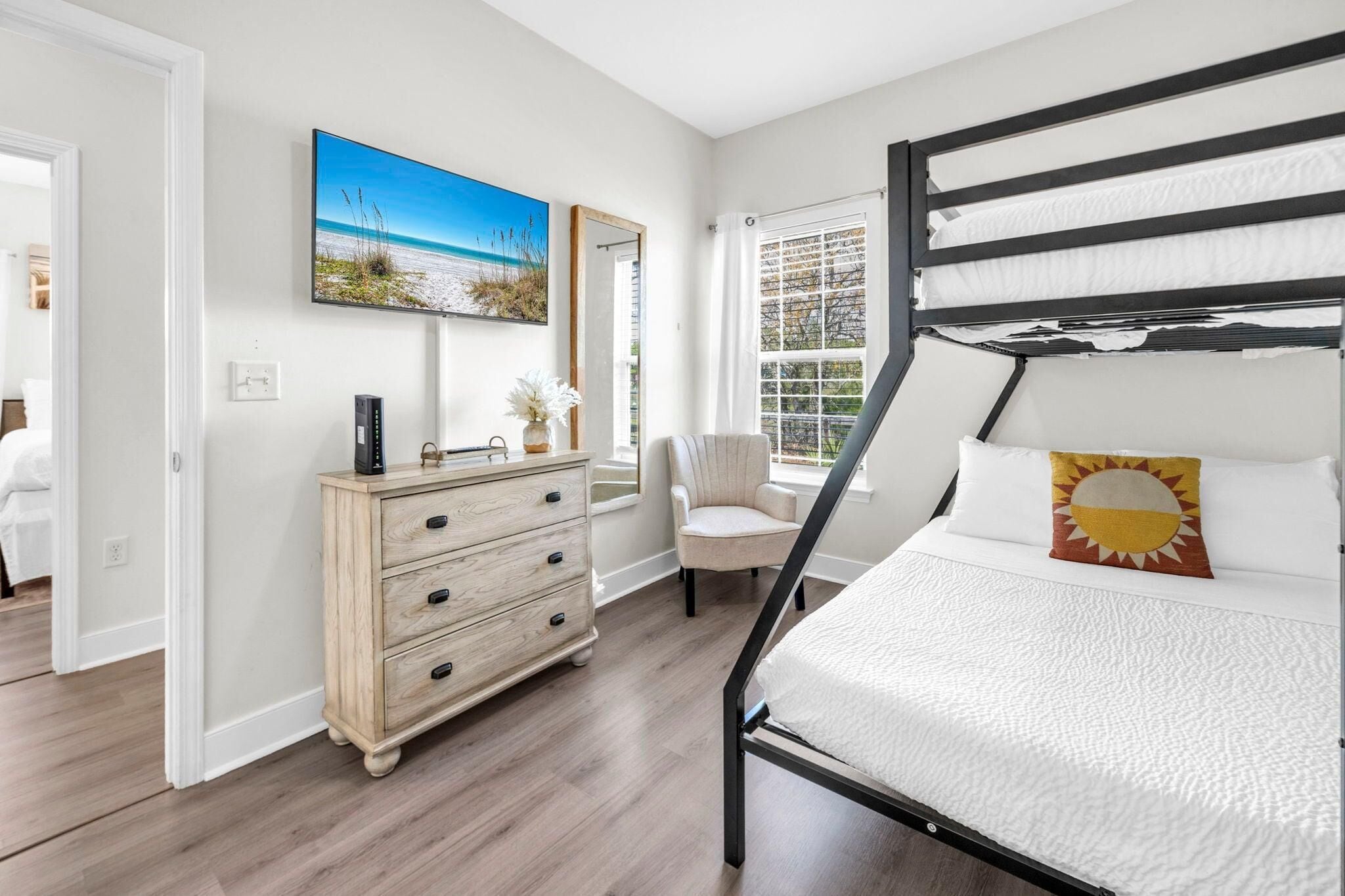 A bedroom with a bunk bed, a dresser, a chair, a television, and a window with a view.