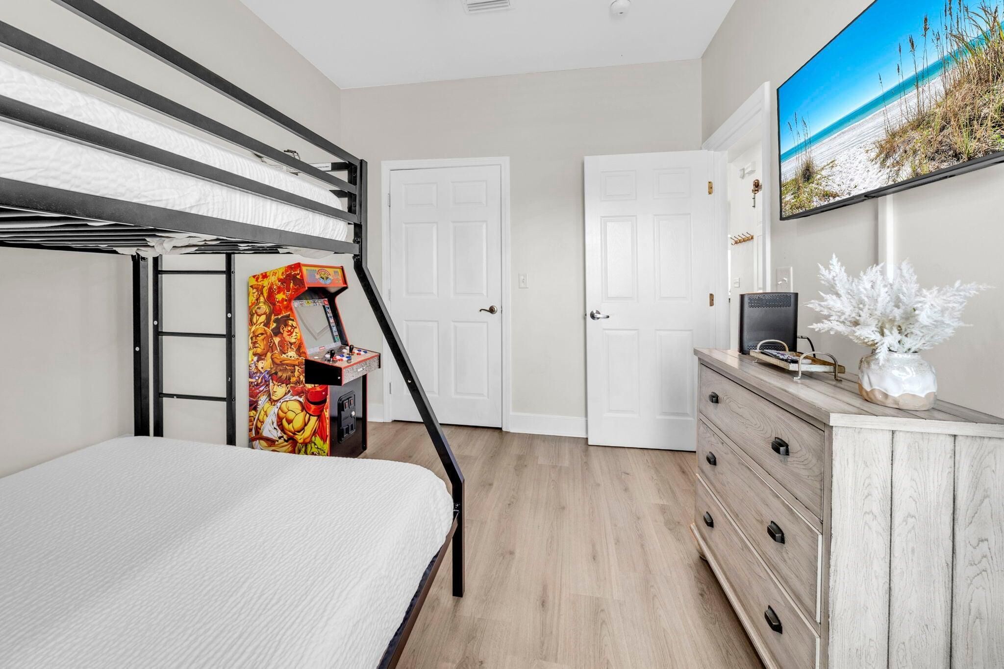 A bedroom with a bunk bed, a desk with a computer, a TV, and a door to another room.
