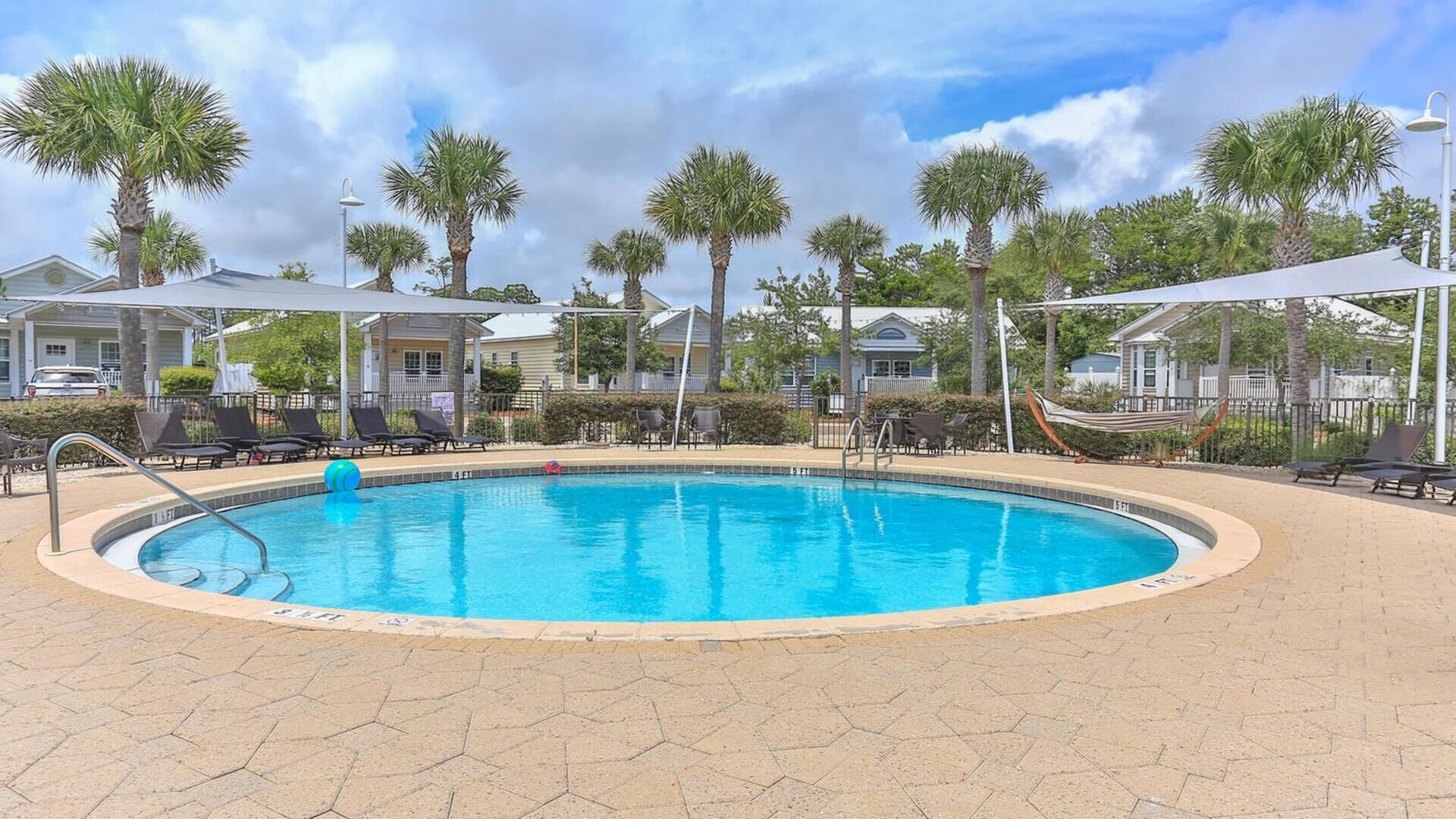 Une piscine circulaire à l’eau d’un bleu limpide, entourée de chaises longues et de palmiers.