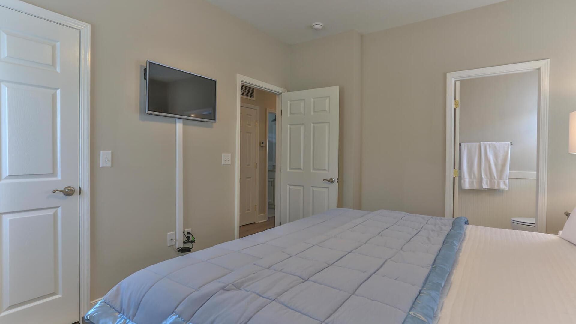 A bedroom with a bed, a TV mounted on the wall, and a door leading to a bathroom.