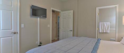 A bedroom with a bed, a TV mounted on the wall, and a door leading to a bathroom.