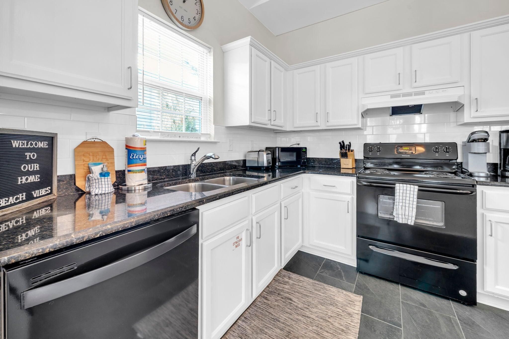 A modern kitchen with white cabinets, a black stove, and a coffee maker.
