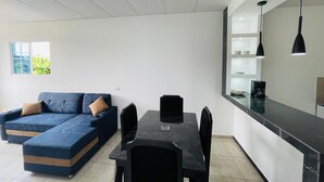 A modern living room with a sectional sofa, a dining table, and a kitchen area with a countertop and pendant lights. - Apartamento Nuevo, Moderno, Acogedor y muy Accesible a Todo en San Salvador (Mejicanos)