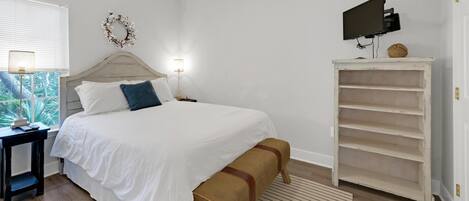 Une chambre à coucher avec un lit, des tables de chevet, une télévision et une armoire blanche.