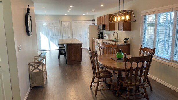 A modern kitchen with wooden cabinets, a central island, and a dining area with wooden chairs. - Family-sized home 5 minutes from beaches & Point Pelee National Park! (Leamington)