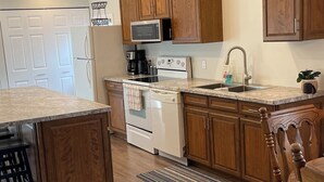 A modern kitchen with wooden cabinets, a white refrigerator, a microwave, a stove, and a sink. - Family-sized home 5 minutes from beaches & Point Pelee National Park! (Leamington)