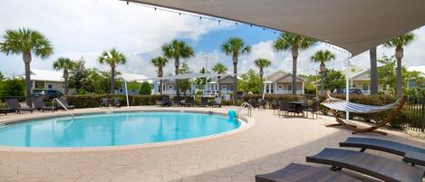 A pool area with lounge chairs, a hammock, and palm trees.