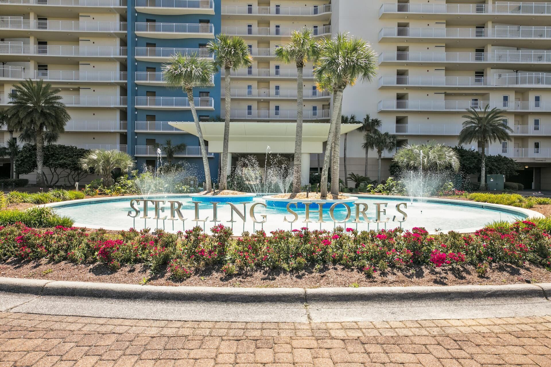 En hotellentrén med en pool, palmer och en skylt med texten ”STERLING SHORES”.