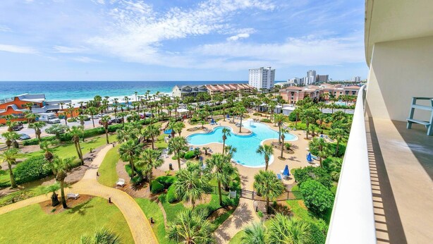 Um resort com uma piscina grande, palmeiras e vista para o oceano.