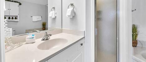 A modern bathroom with a white sink, a mirror, a glass shower enclosure, and a potted plant.