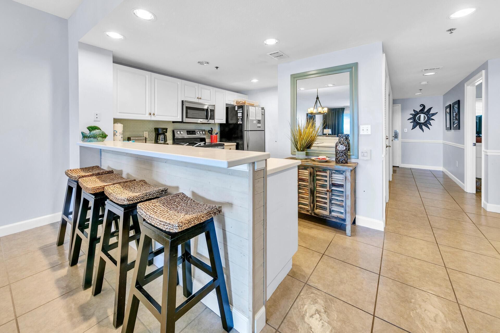A modern kitchen with white cabinets, a central island with stools, and a dining area with a view of the living room.