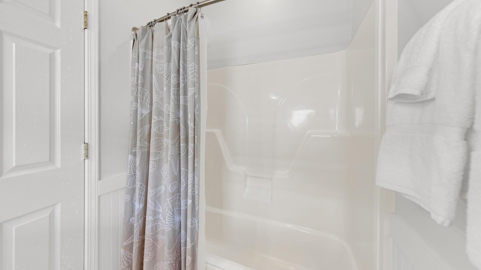 A bathroom with a shower curtain, a white bathtub, and a towel hanging on the wall.