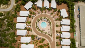 Vista aérea de un complejo turístico con piscina central, villas distribuidas y un camino sinuoso.