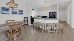 Una cocina moderna con armarios blancos, un refrigerador negro y una mesa de madera con cuatro sillas.