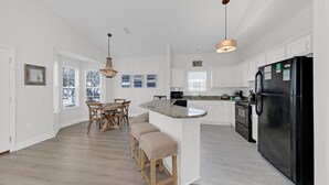 Una cocina moderna con armarios blancos, un refrigerador negro y una zona de comedor con sillas y una mesa de madera.