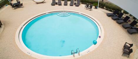 A circular pool with a surrounding lounge area, including chairs and tables.