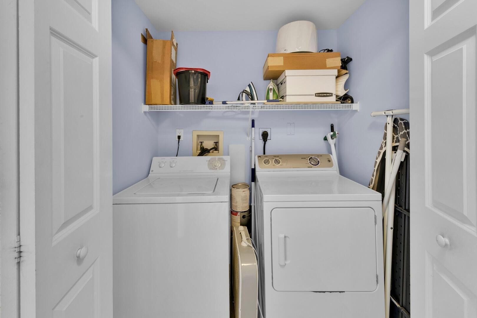 A laundry room with two washing machines, a shelf with cleaning supplies, and a giraffe-patterned item on the right.