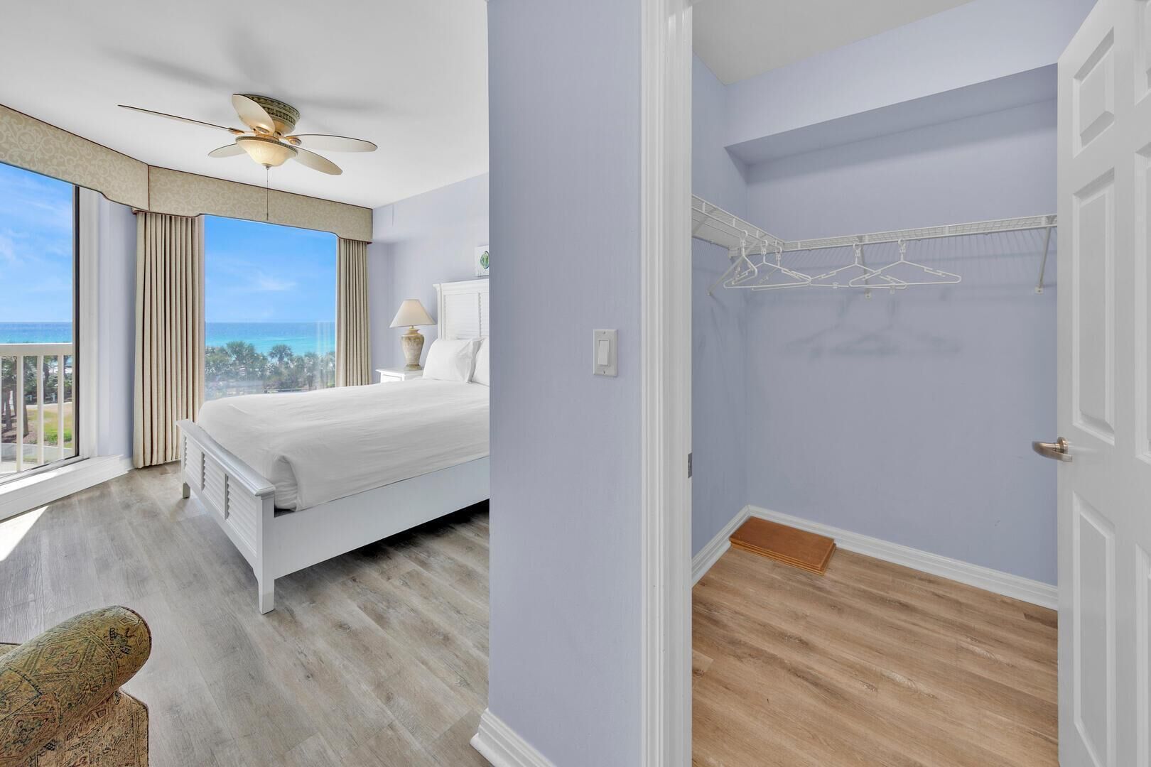 A bedroom with a bed, a nightstand, a lamp, a ceiling fan, and a view of the ocean.
