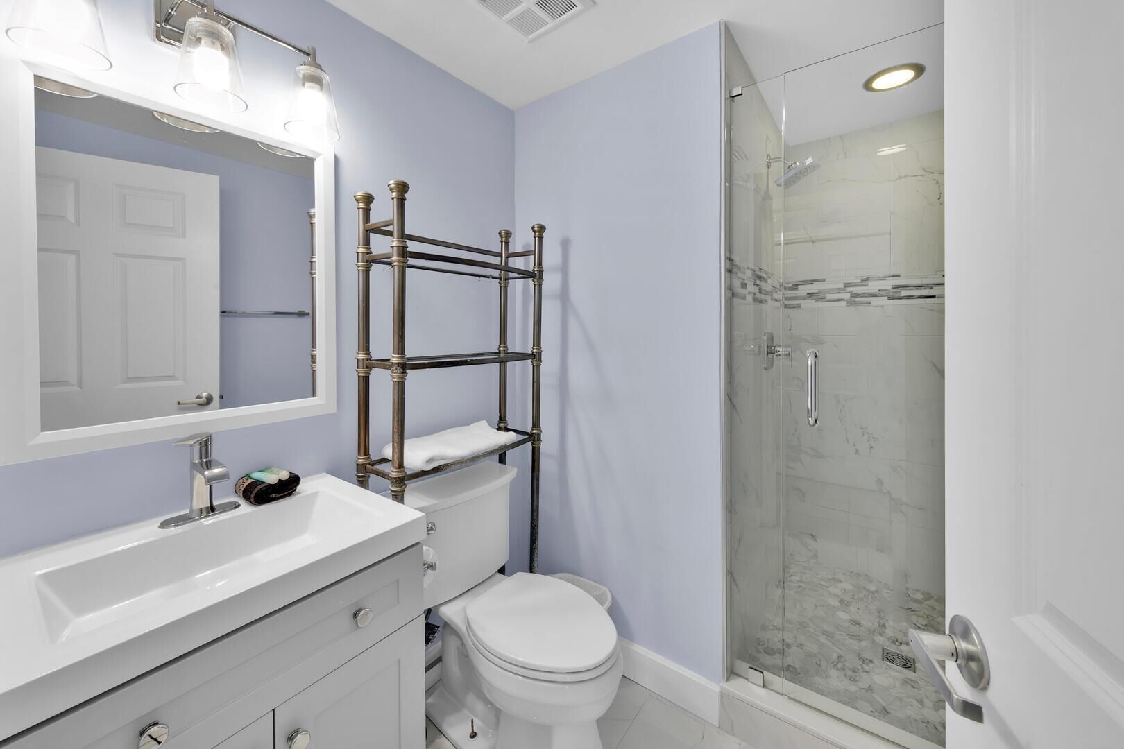A bathroom with a white vanity, a glass shower enclosure, and a wooden shelf unit.