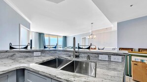 Una cocina moderna con una isla grande, pileta de acero inoxidable y vista al océano a través de amplias ventanas.