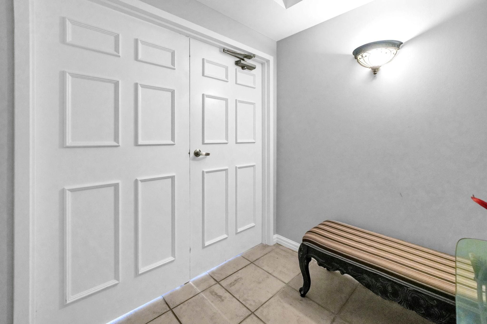 A hallway with a white door, a bench, and a wall-mounted light fixture.