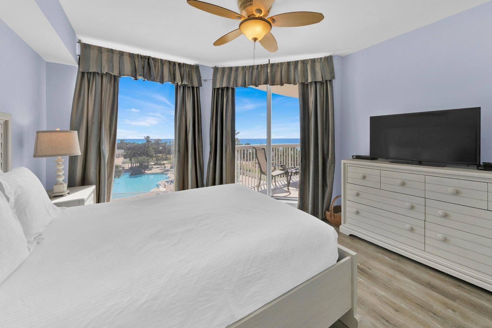 Une chambre d’hôtel comprenant un lit, une télévision, une commode et un balcon avec vue sur une piscine et des palmiers.