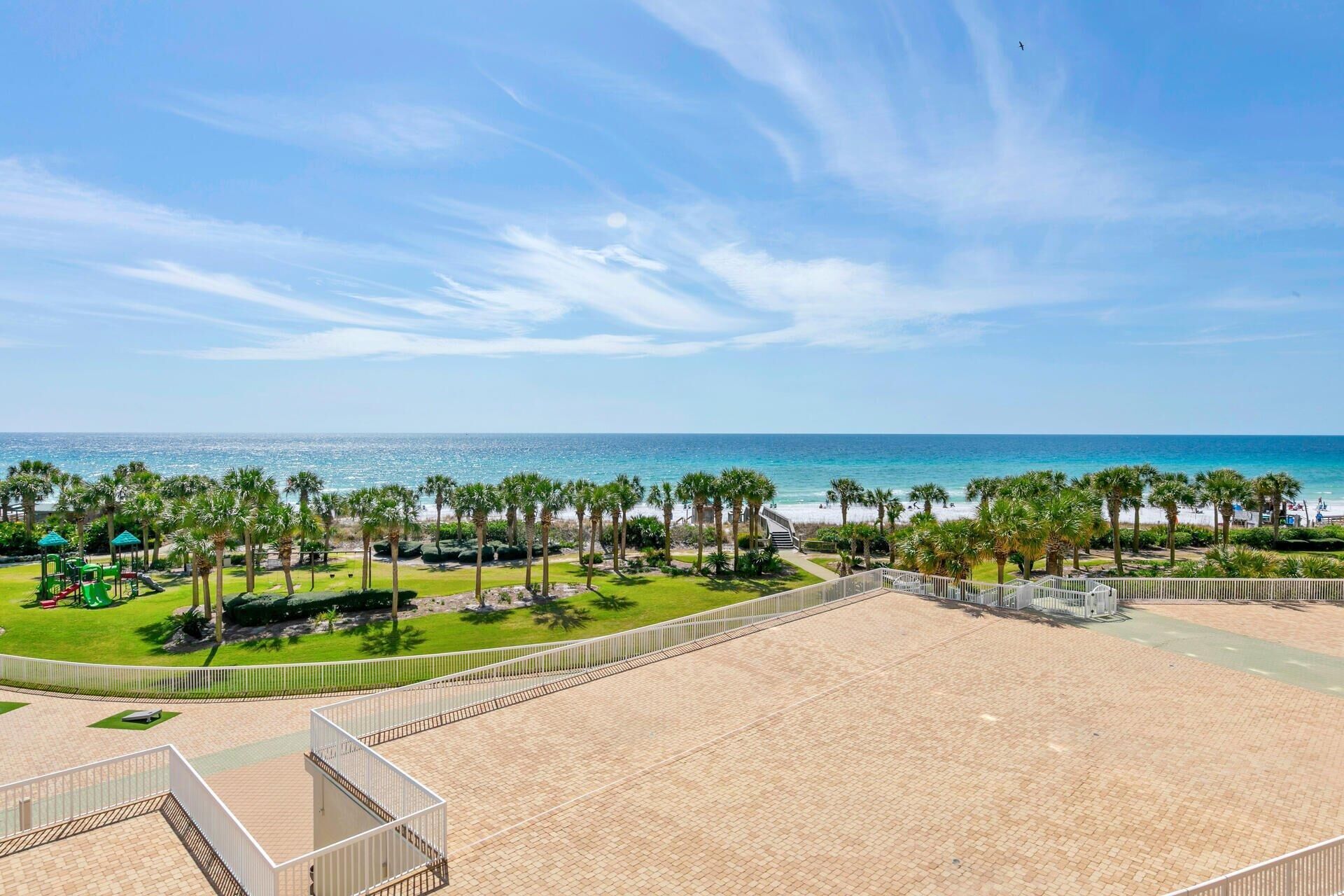 Une plage avec vue sur la mer, une zone délimitée par une clôture, des palmiers et un espace de jeux pour enfants.