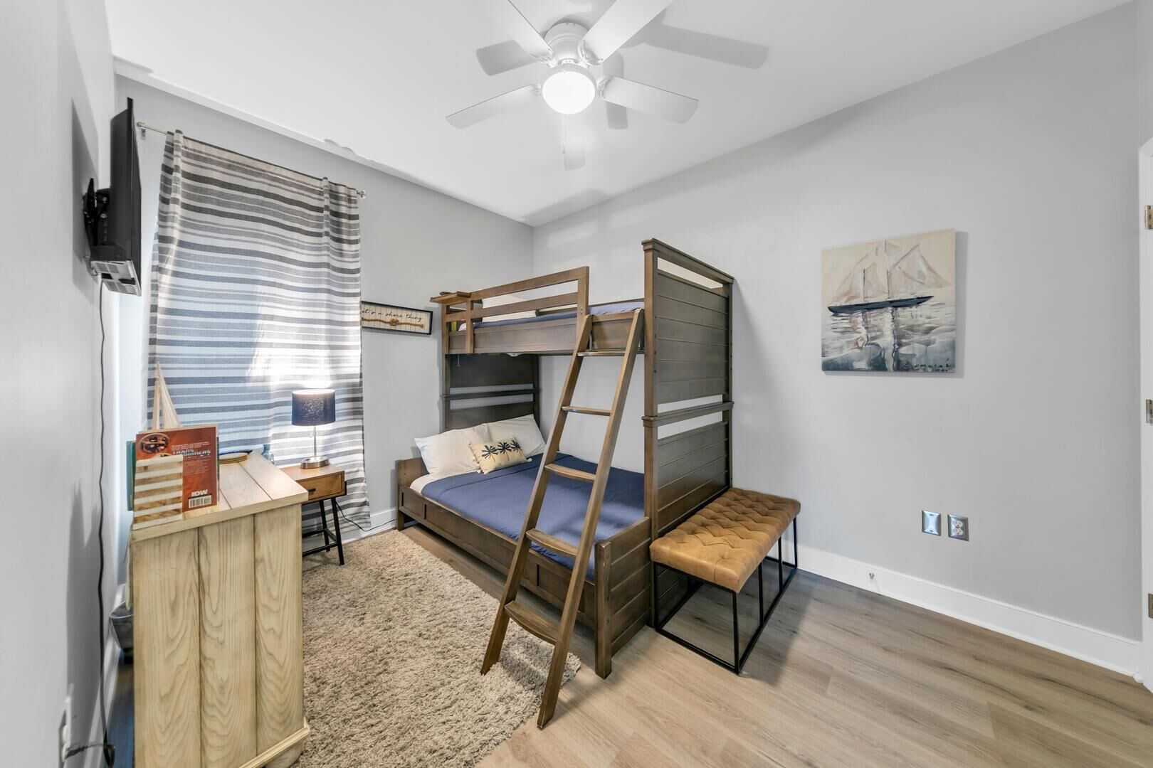 A bedroom with a bunk bed, a desk, a chair, a lamp, and a ceiling fan.