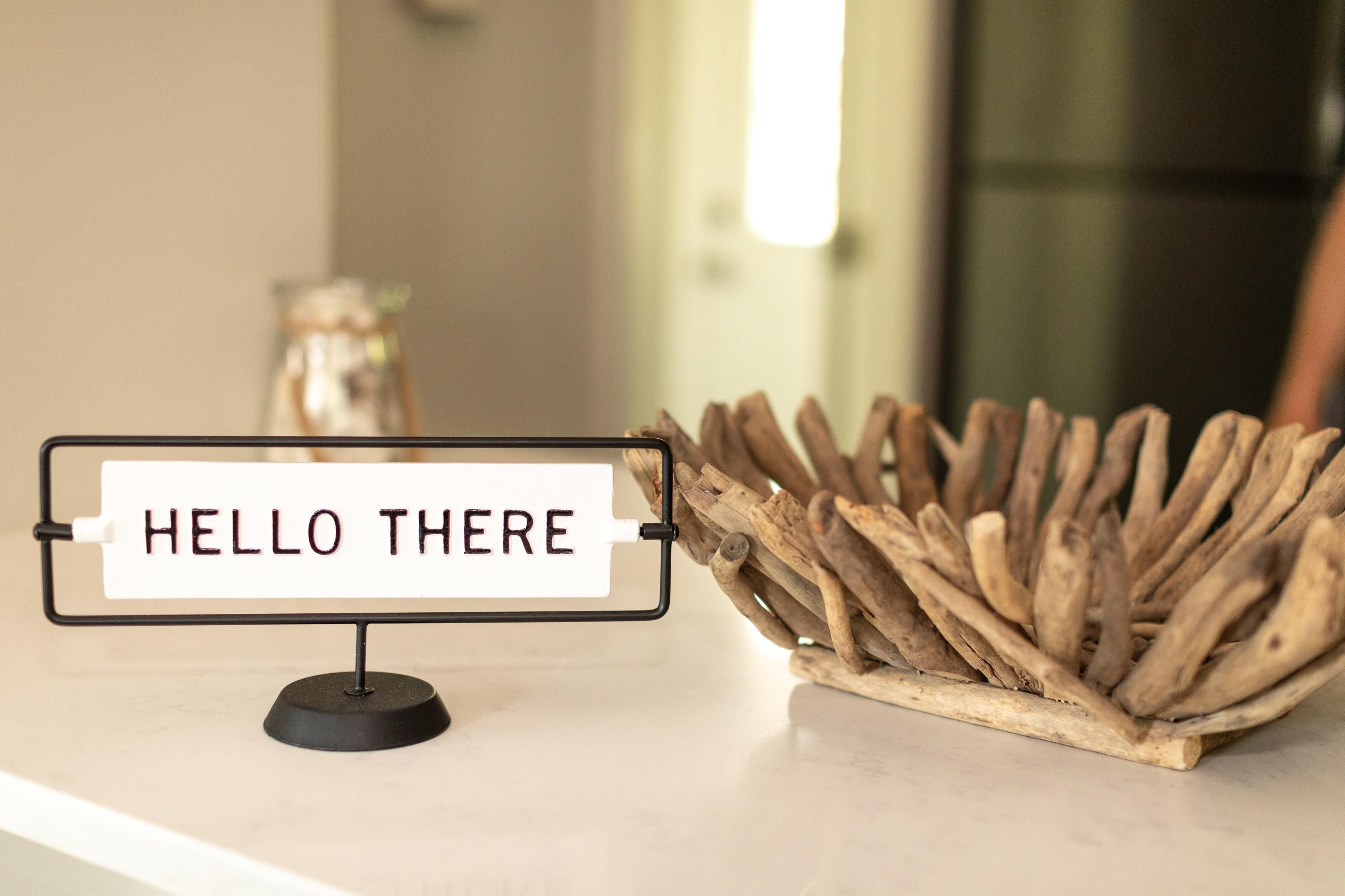 A sign with the text "HELLO THERE" on a stand, next to a rustic wooden structure.