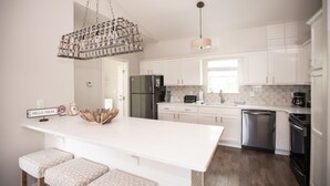 Una cocina moderna con armarios blancos, una isla central, electrodomésticos de acero inoxidable y una lámpara colgante.