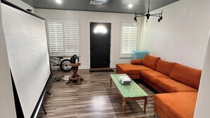 A room with a whiteboard, a bicycle, an orange couch, and a projector on a green table. - Hidden gem. Tiny home in mural district.  (Blythe)