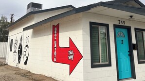 A building with a white exterior, a blue door, and a red arrow sign pointing to the right. - Hidden gem. Tiny home in mural district.  (Blythe)