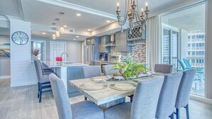 A modern kitchen with a central island, pendant lighting, and a dining area with a wooden table and gray upholstered chairs. - St. Maarten 701 at Silver Shells (Destin)
