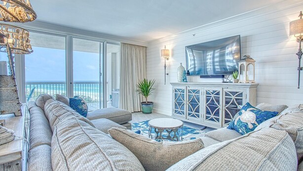 A spacious living room with a large sofa set, a coffee table, and a TV mounted on the wall. There is a potted plant and a decorative cabinet with glass doors. - St. Maarten 701 at Silver Shells (Destin)
