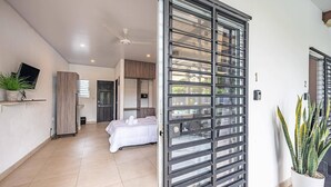 A modern hotel room with a bed, a TV, a ceiling fan, and a sliding glass door leading to a balcony. - Gorgeous Studios in the heart of Jaco. (Jacó)
