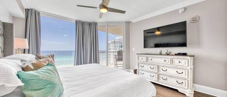 A bedroom with a large bed, a ceiling fan, a TV, and a view of the ocean.