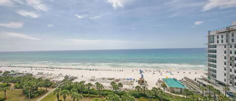 A beach view with a hotel in the foreground, a sandy beach, and a clear sky.
