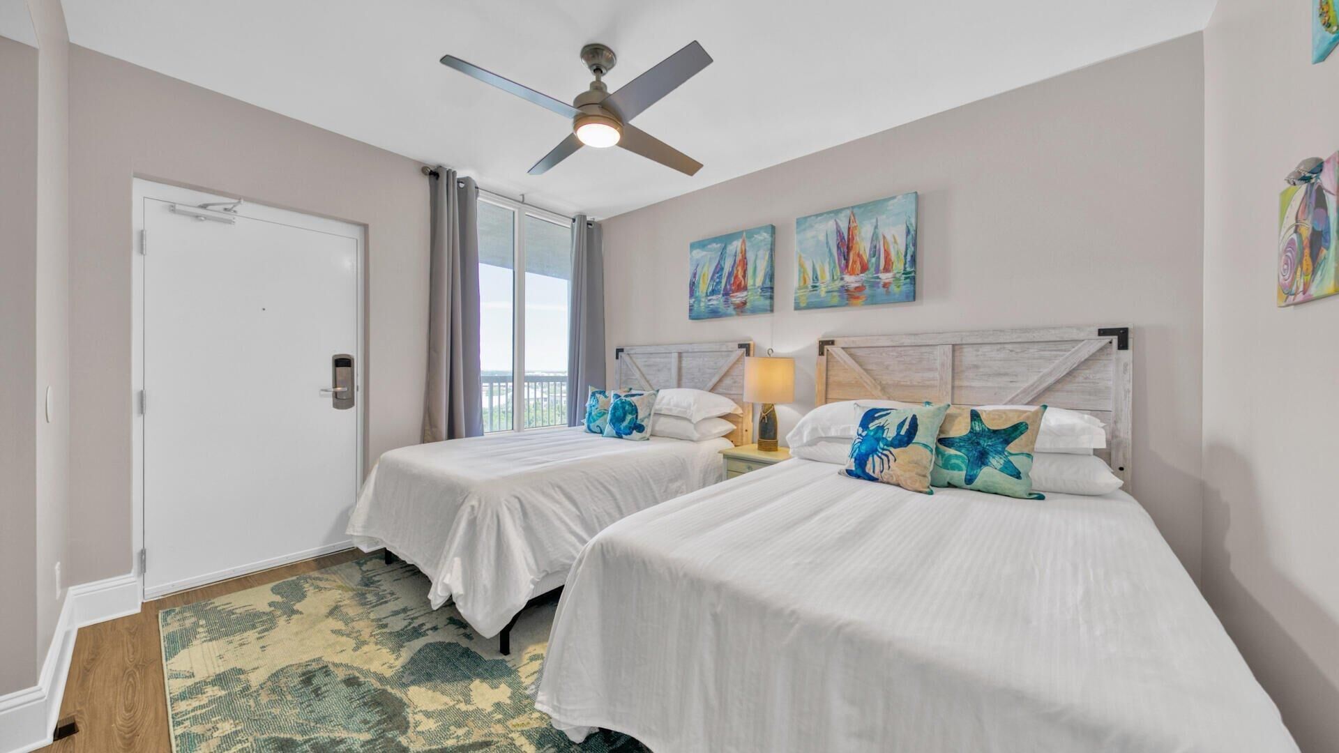 A hotel room with two beds, a ceiling fan, a door, and a window with curtains.