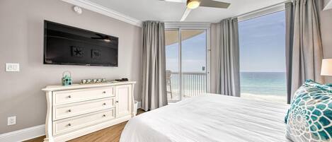 Un dormitorio con una cama grande, un ventilador de techo, un televisor, un aparador y un balcón con vista al océano.