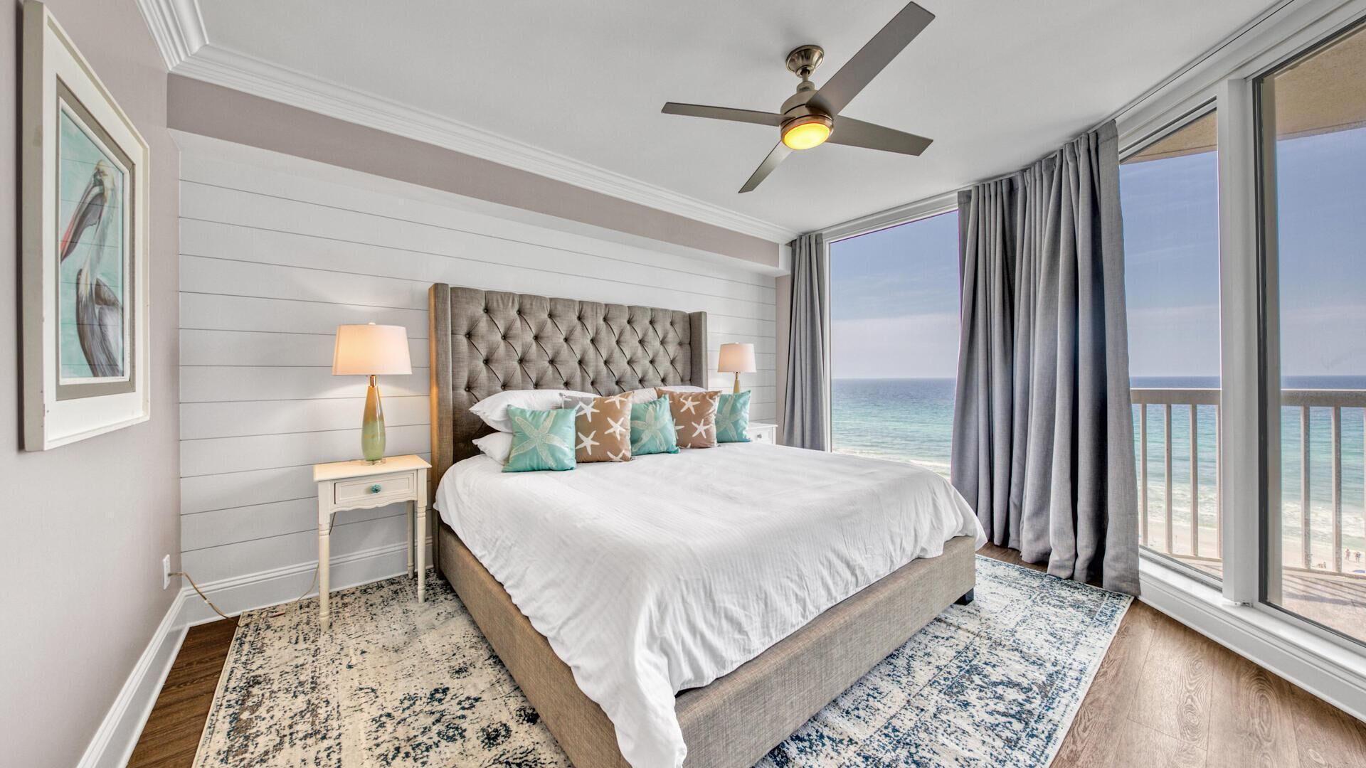 Een slaapkamer met een groot bed, een plafondventilator, een nachtkastje met lamp en uitzicht op de oceaan.
