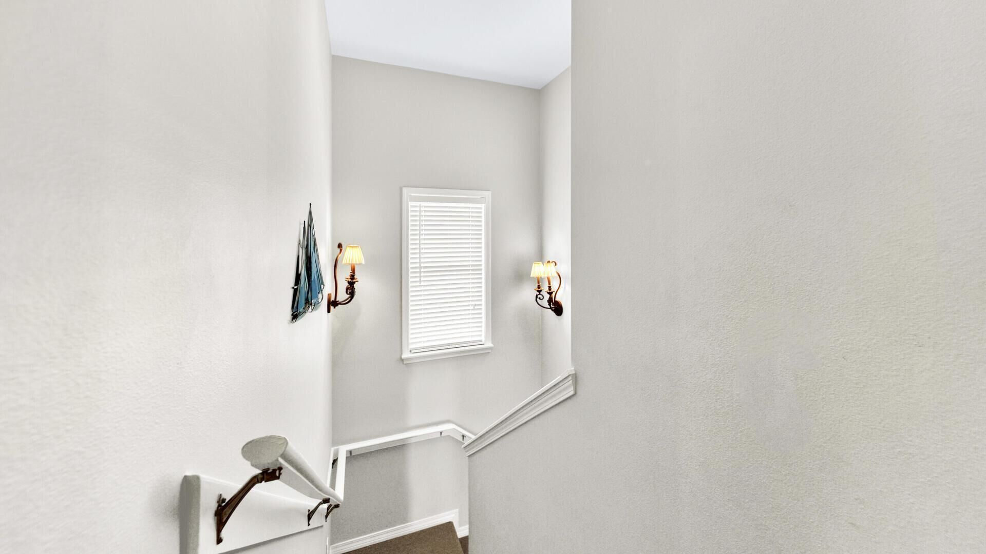 Una escalera con barandilla blanca, un aplique en la pared y una ventana con persianas.