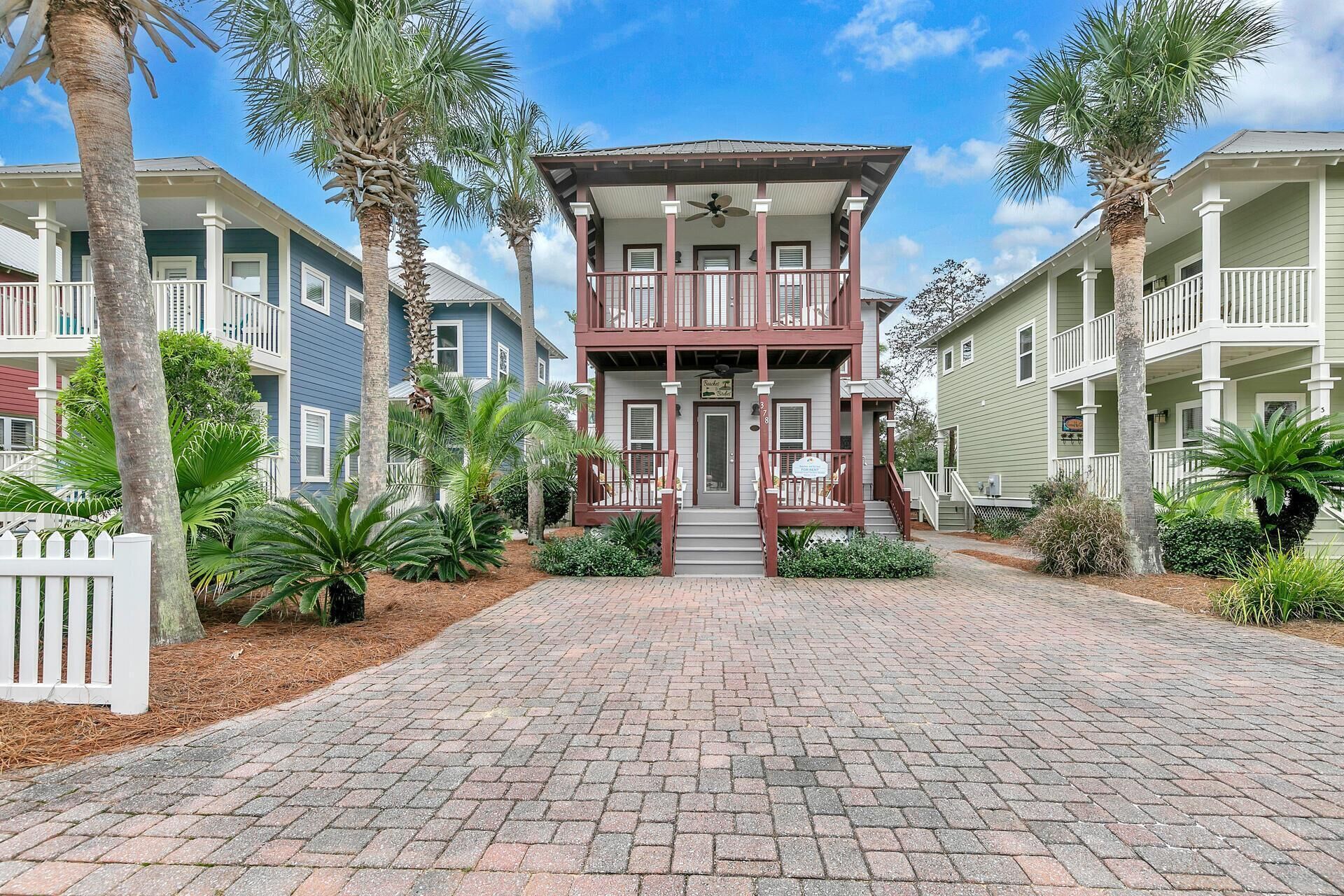 A two-story building with a central entrance, surrounded by palm trees and a brick pathway.