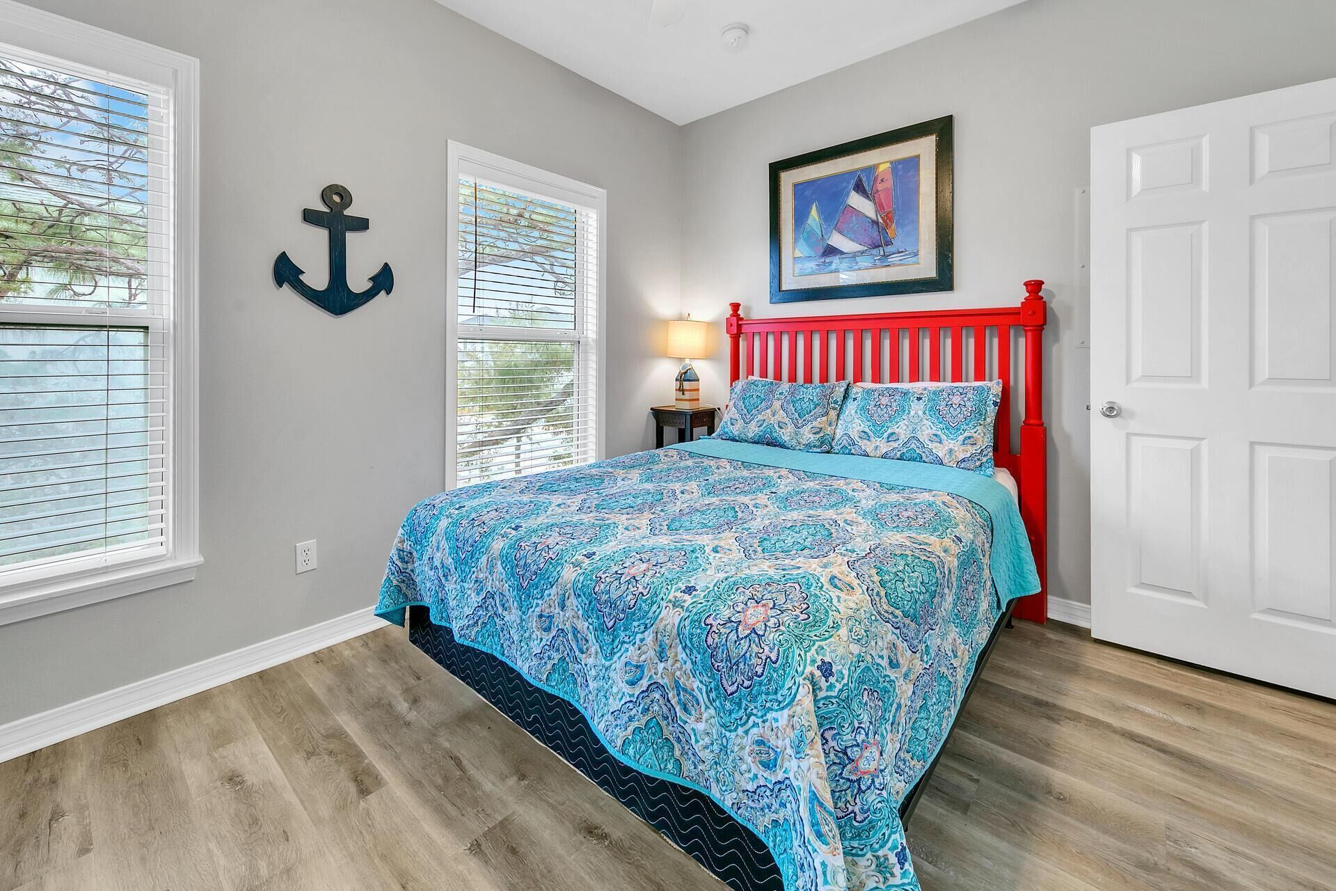 A bedroom with a bed, a nightstand, a lamp, a framed painting, and a door.
