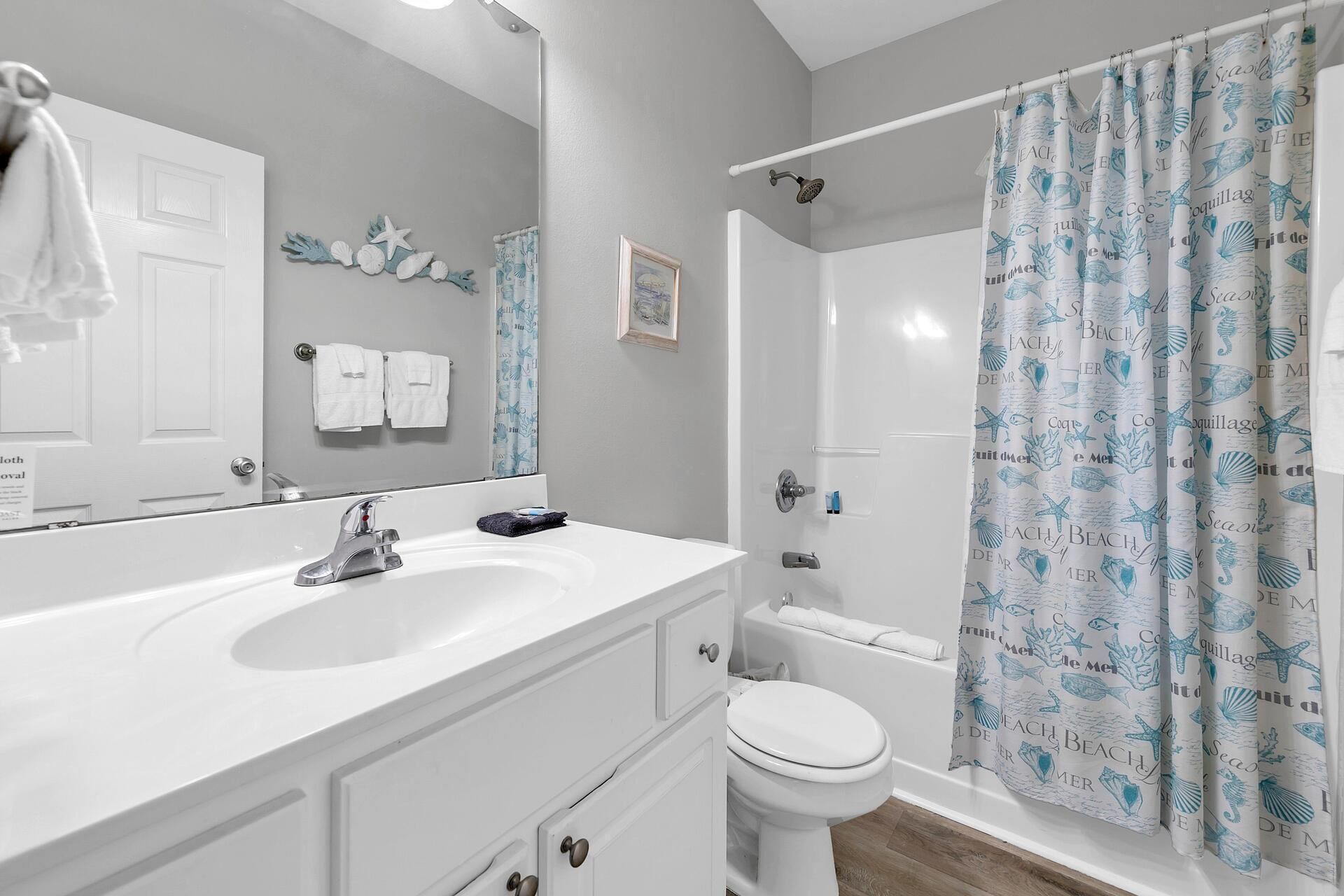 A bathroom with a white sink, mirror, and toilet. There is a shower curtain with a sea theme.