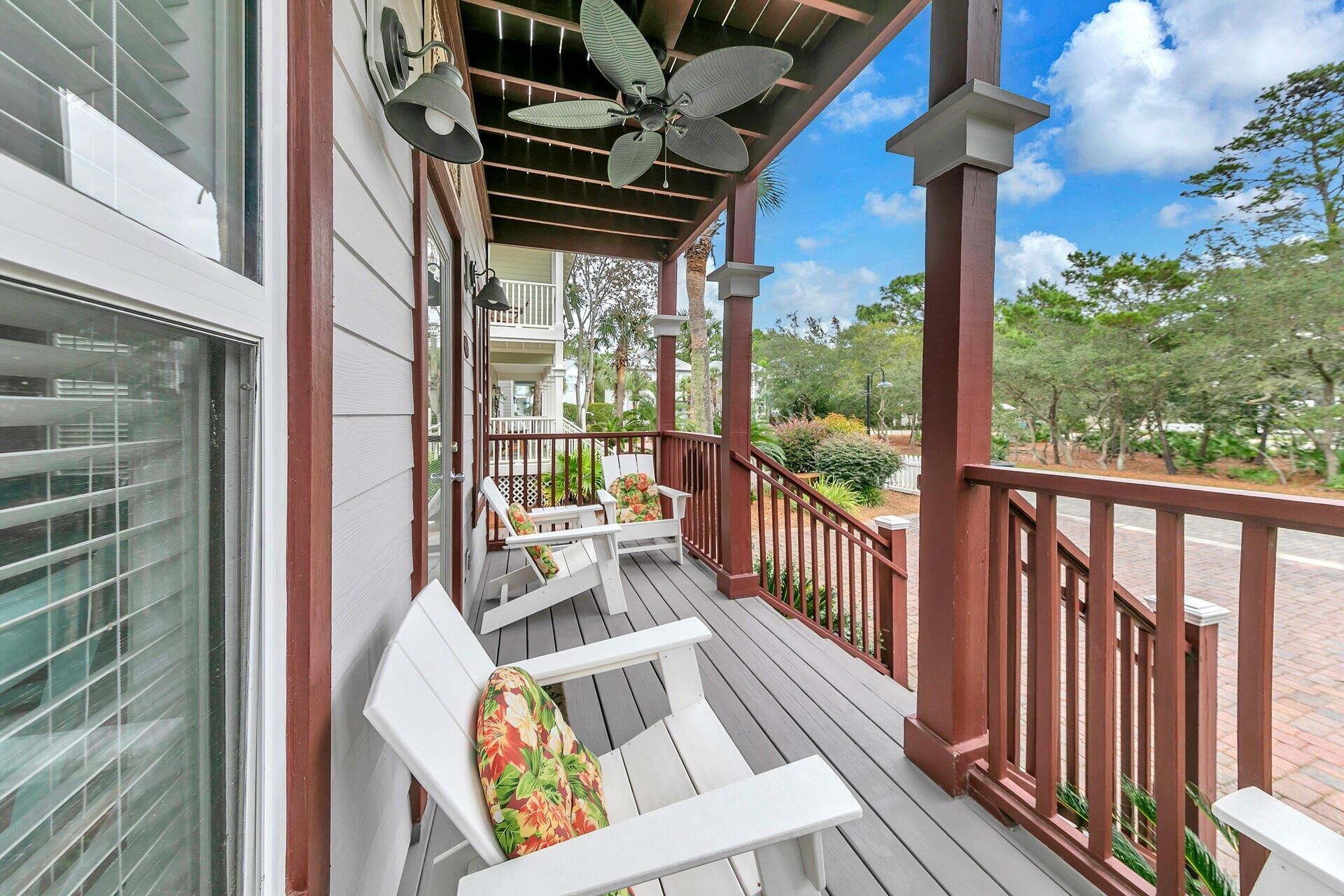 A covered porch with white chairs and a ceiling fan.