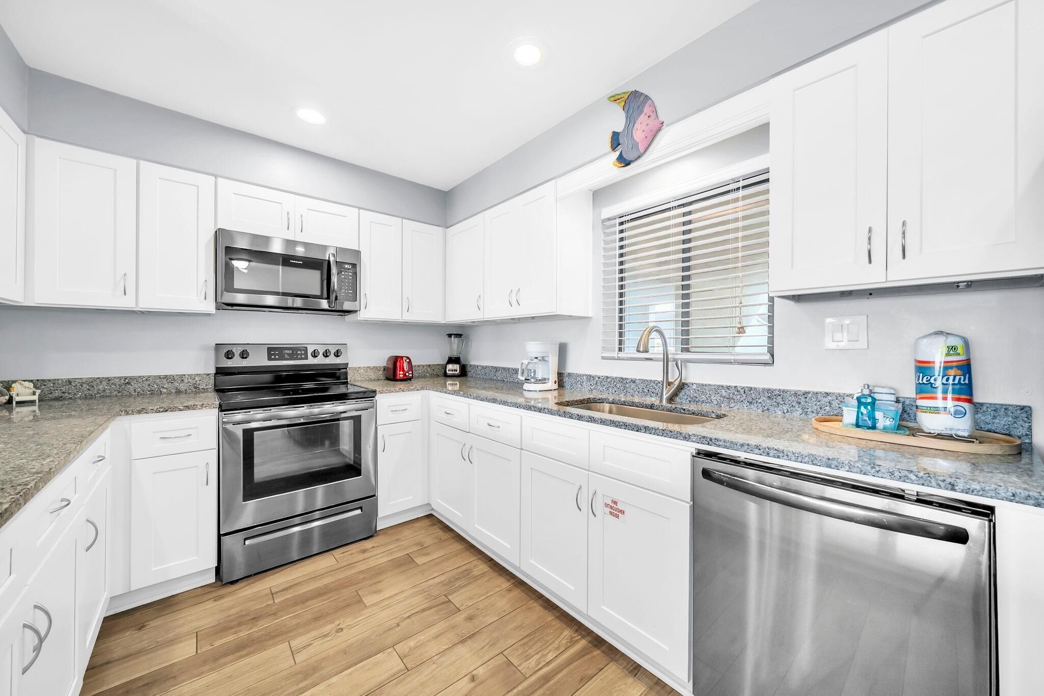 A modern kitchen with white cabinets, stainless steel appliances, a granite countertop, and a wooden floor.